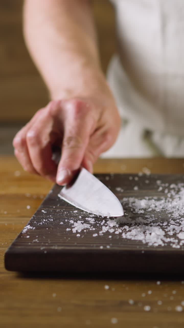 Male chef shakes salt out off delicious fat pickled herring above cutting board at kitchen table close view. Healthy nutrition of seafood