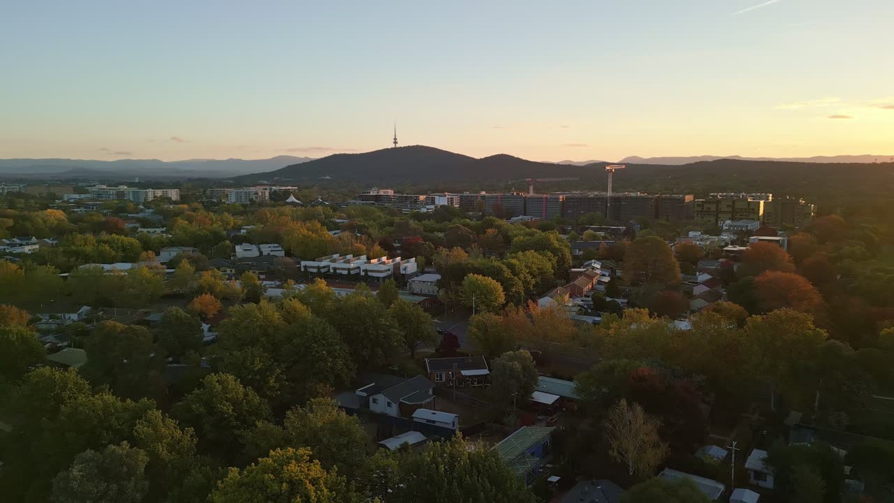 Late afternoon drone shot over Canberra’s suburbs, with the iconic tower in the distance and cranes marking urban development.