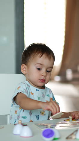 cute little toddler plays with toy sitting at desk. lovely boy collects puzzles and claps hands happily. vertical video
