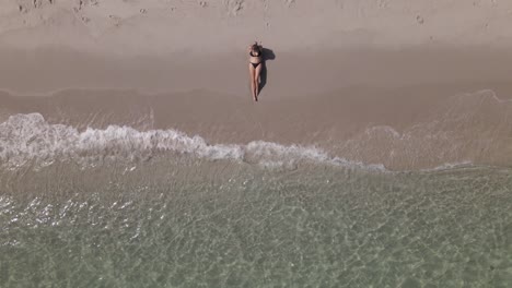 vertical aerial: young caucasian woman in bikini on warm sandy beach