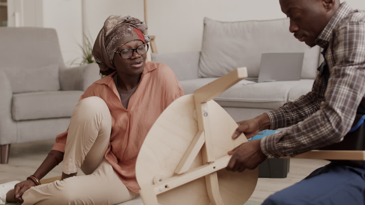 Young African-American Housewife Watching Carpenter Assembling Chair