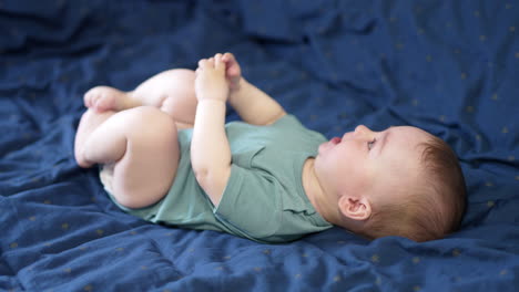 lovely caucasian baby boy lies on bed with bare feet. cute kid rising legs up and mumbling something.