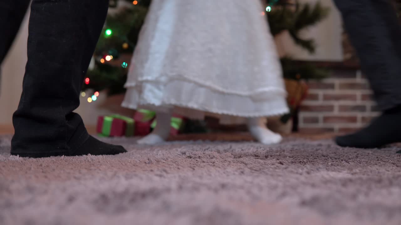 크리스마스 트리에서 크리스마스를 위해 둥근 춤을 추는 가족의 클로즈업 다리. 할아버지, 할머니, 손녀가 새해를 축하합니다.