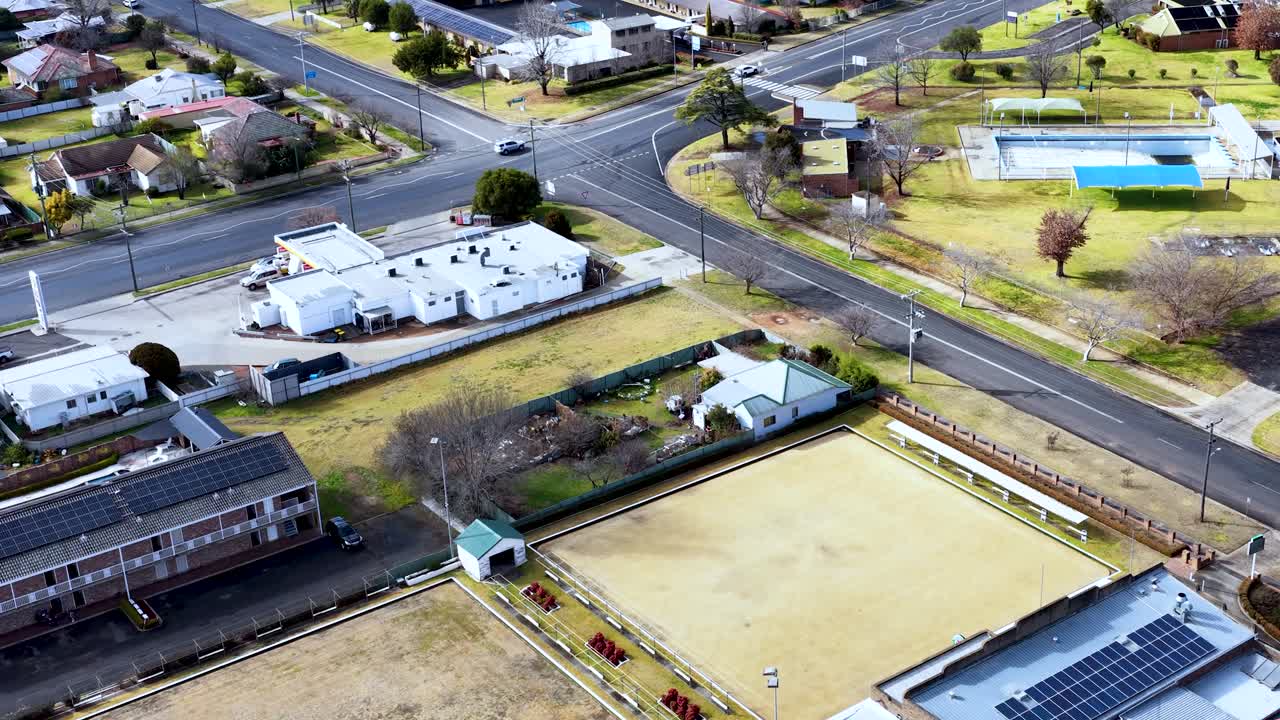 Drone footage captures a bright, daytime aerial view of Coonabarabran’s residential streets, buildings, and sports fields, with smooth forward camera movement and clear lighting