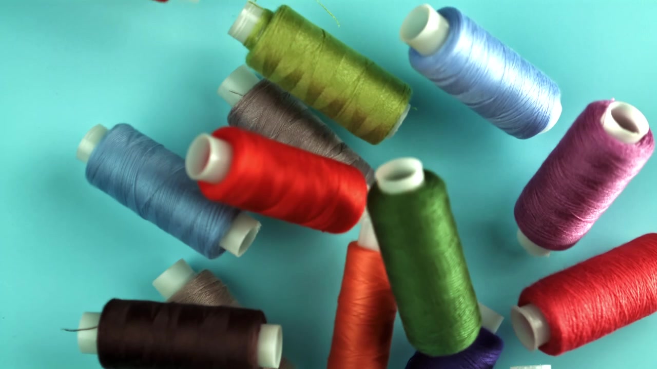 Colorful Spools of Sewing Thread Falling onto a Blue Background