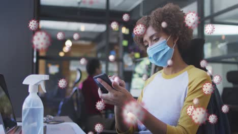 Animación-De-19-Células-Covid-Sobre-Una-Mujer-Limpiando-Un-Teléfono-Inteligente-En-La-Oficina-Con-Mascarilla