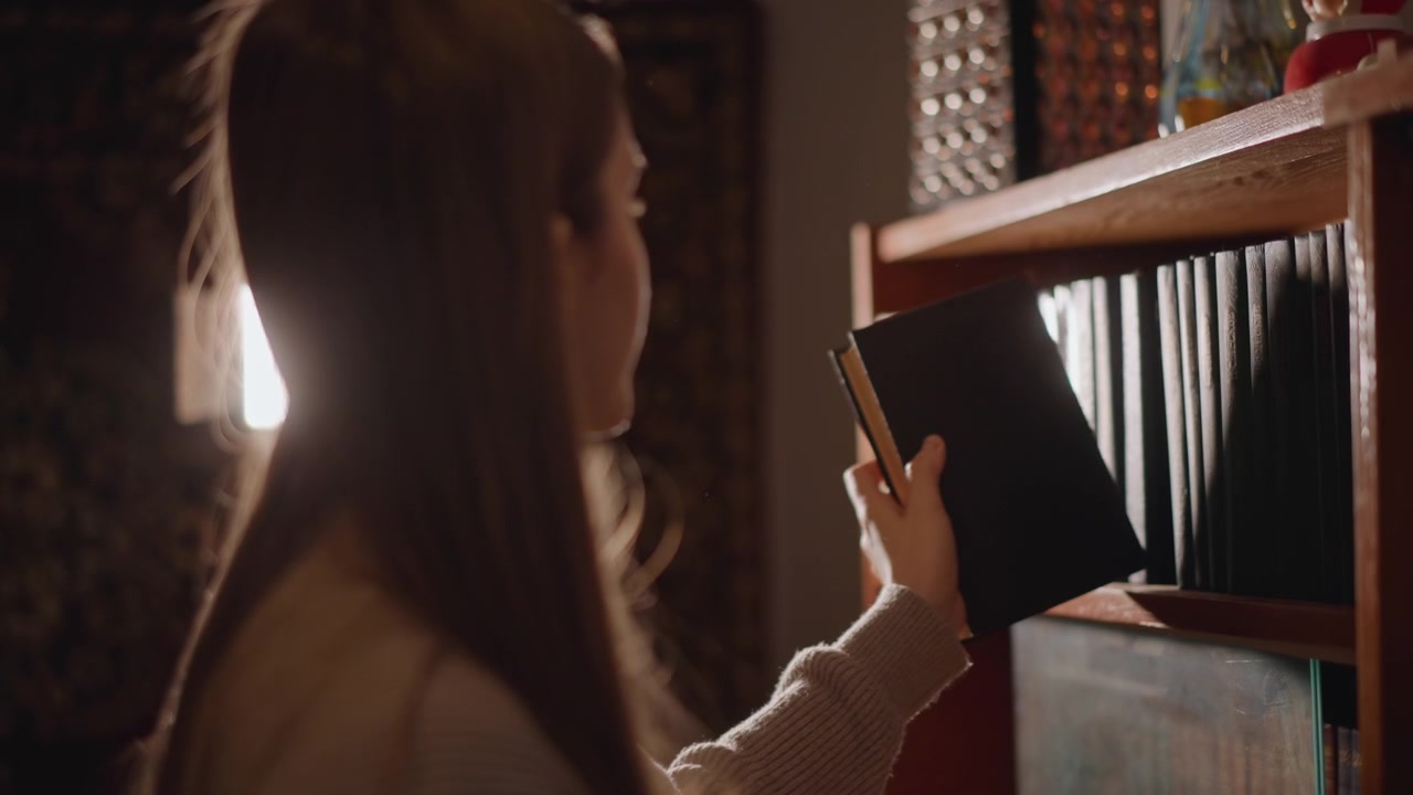 Donna bianca che esamina attentamente una libreria. Giovane donna dalla pelle bianca che esplora calorosamente i dorsi di libri vintage. Adolescente con un maglione che seleziona libri molto amati in un'accogliente ambientazione cinematografica.