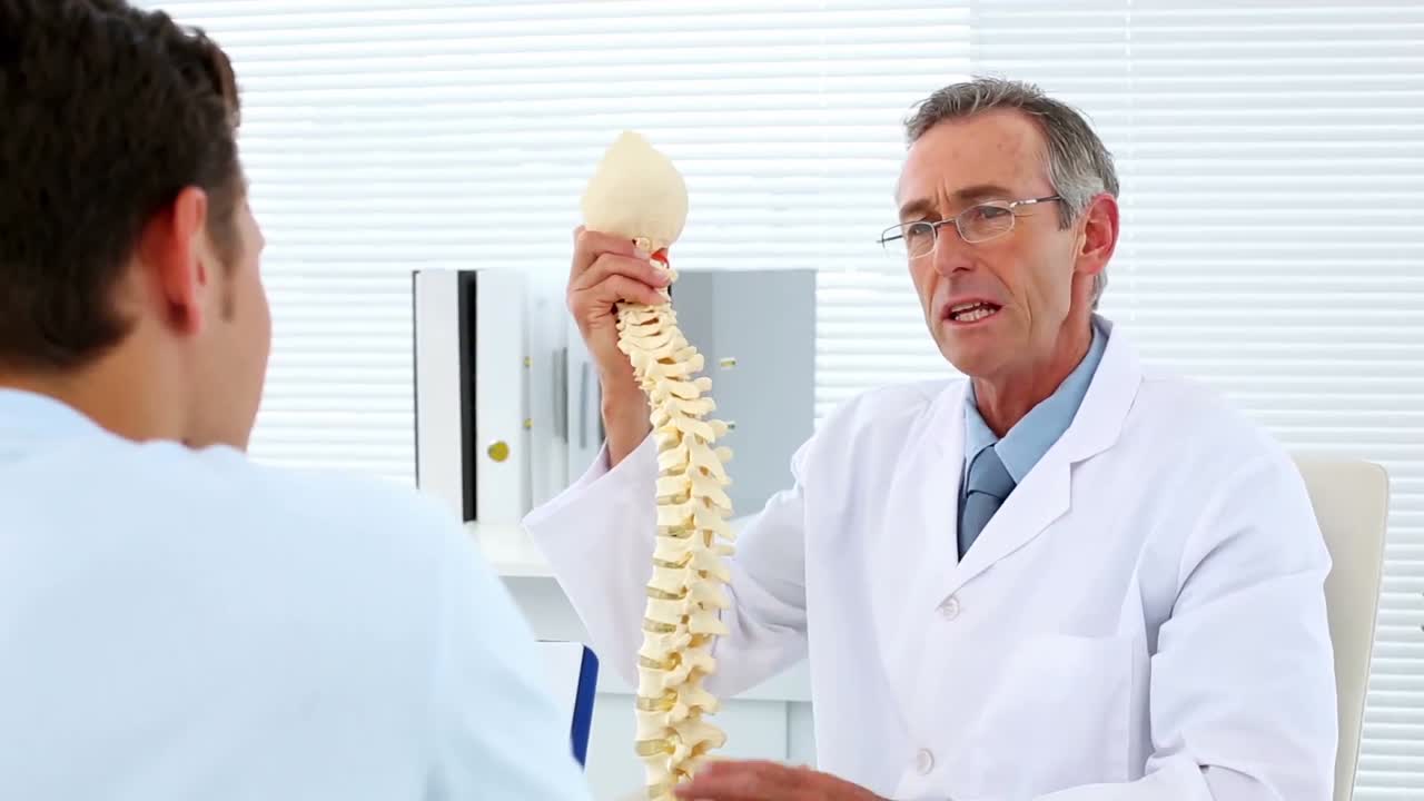 médico maduro explicando a su paciente sobre el modelo de la columna vertebral