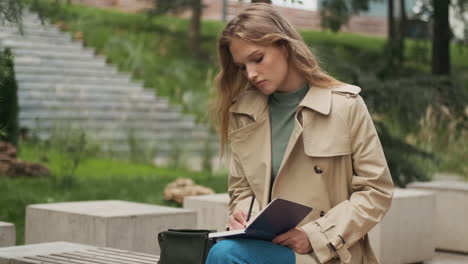 estudiante caucásica escribiendo en un cuaderno en el parque.