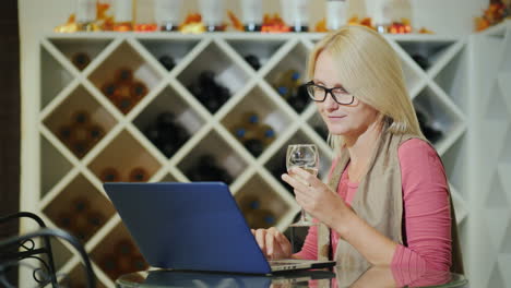 Mujer-Cata-Vino-Sentado-En-Una-Mesa-En-Una-Bodega-Usando-Una-Computadora-Portátil