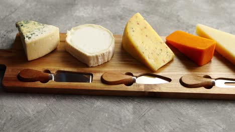 Assortment-of-various-kinds-of-cheeses-served-on-wooden-board-with-fork-and-knives