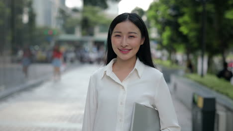 young asian businesswoman smiling outdoors with laptop