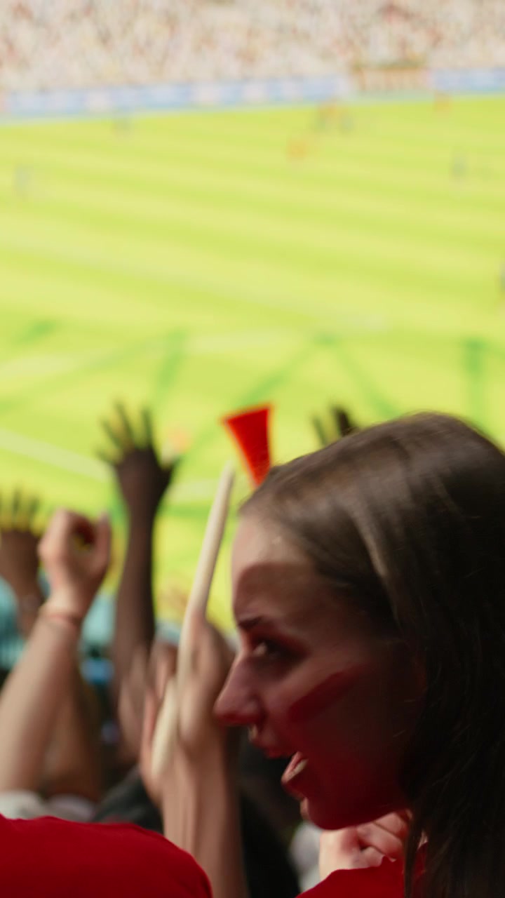 Vertikal video: Fotballsupportere bakfra med tromme og røde skjerf ser på direktesendt kamp.