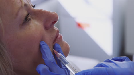 mujer madura sentada en una silla recibiendo una inyección de botox por una doctora