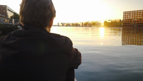 Video-behind-a-young-man-shoulder-looking-into-the-sunset-sitting-on-a-pier-in-Amsterdam