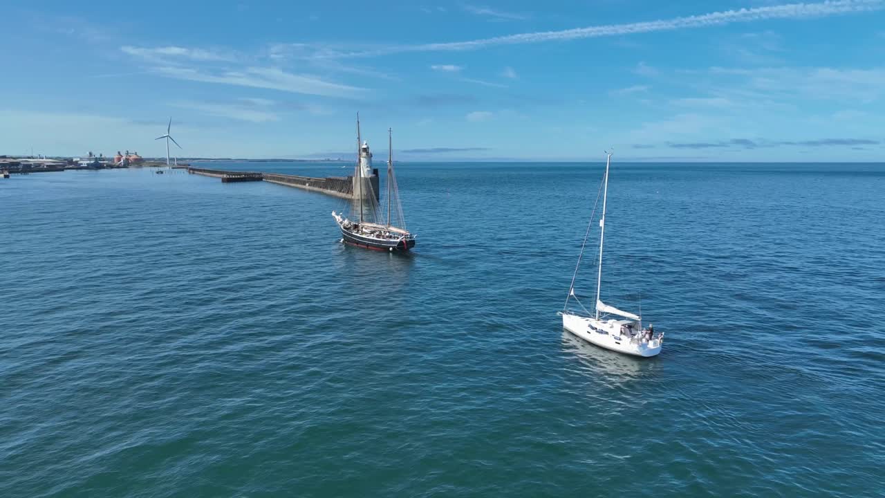 Two very different boats sailing into harbour, one modern yacht and one traditional tall ship