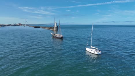 two very different boats sailing into harbour, one modern yacht and one traditional tall ship