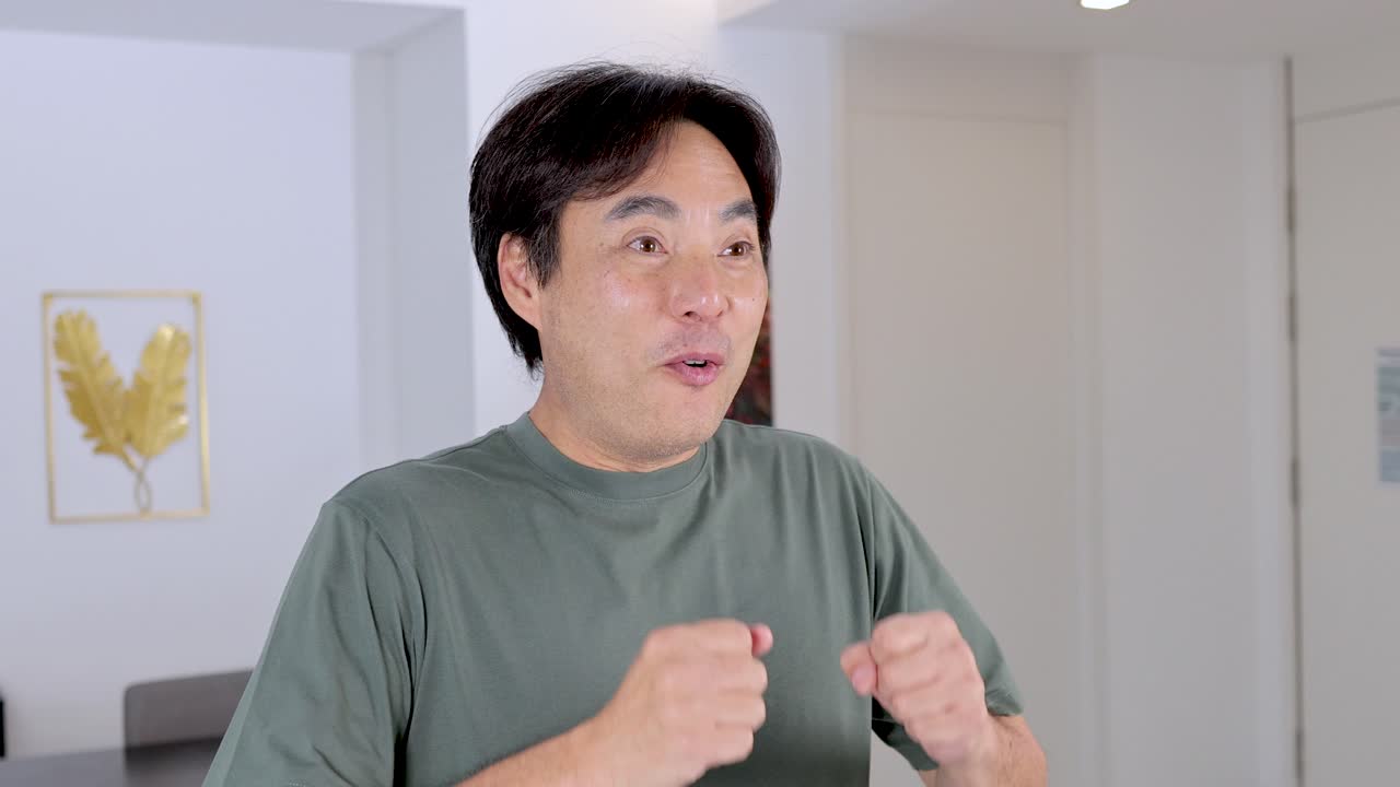 Smiling Asian man performs excited, surprised facial expressions and gestures in bright, modern interior