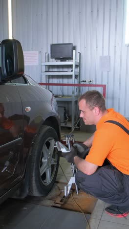 Mechanic Performing Wheel Alignment on a Car in a Garage