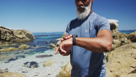 senior african american man exercising using smartwatch on rocks by the sea