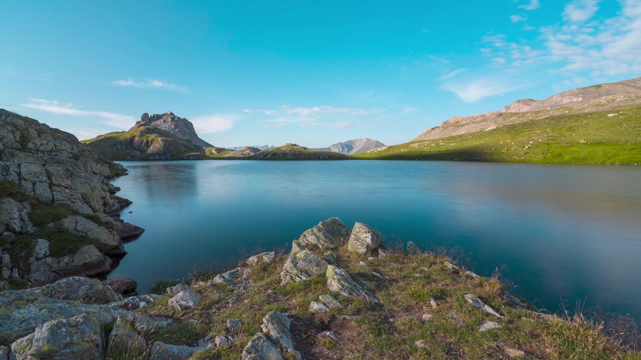 Rocas escarpadas bordean la orilla del Lago Superiore di Roburent mientras tranquilas aguas alpinas reflejan picos distantes bajo la luz del día