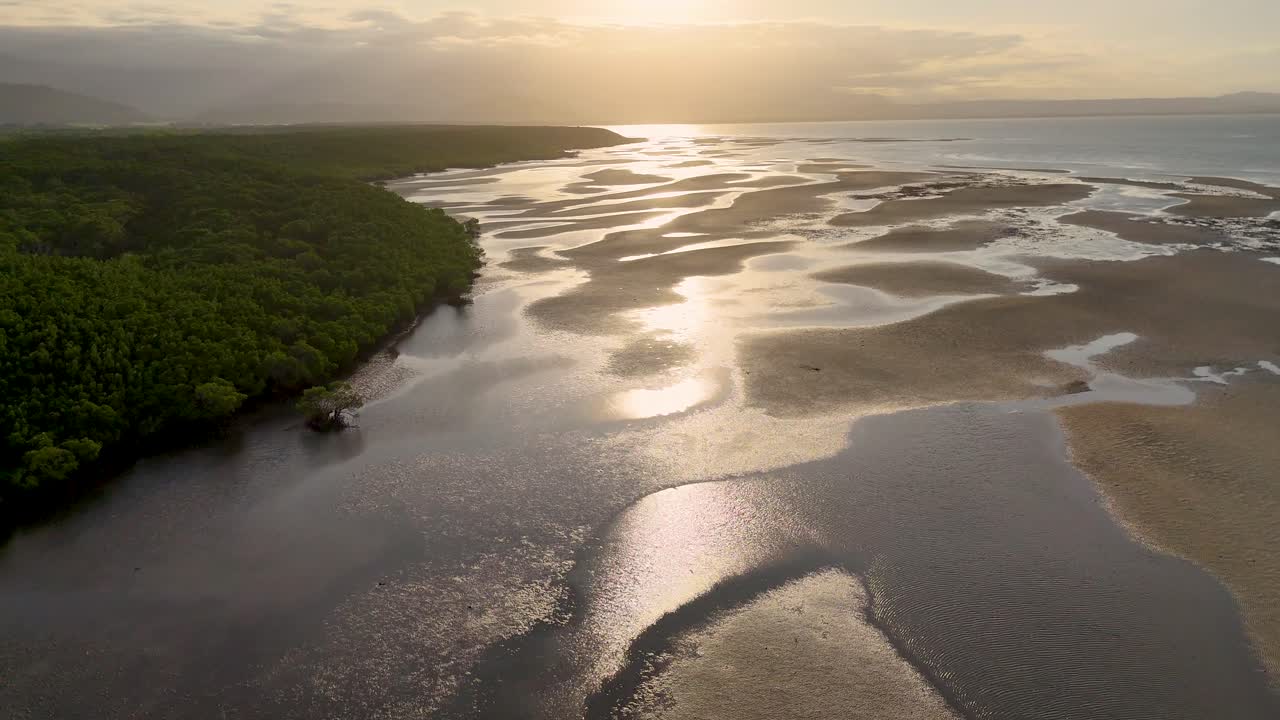 Drone captures serene aerial views of Port Douglas' tidal flats and mangroves at sunset, highlighting reflective water pools and lush greenery