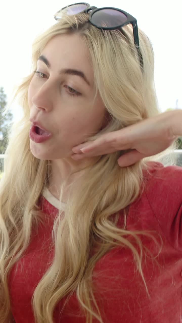 Vertical video: Leaning brunette holding phone, taking selfie with smiling blonde friend on balcony