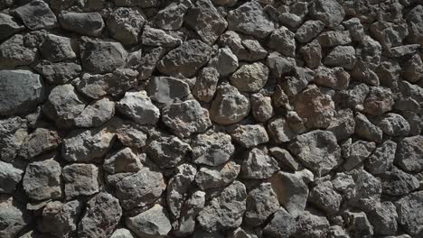 Slide-down,-Uncut-rough-stone-wall-with-concrete-visible-among-the-boulders,-natural-sunlight