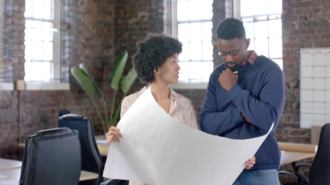 Diverse architect colleagues discussing work and holding blueprints in slow motion