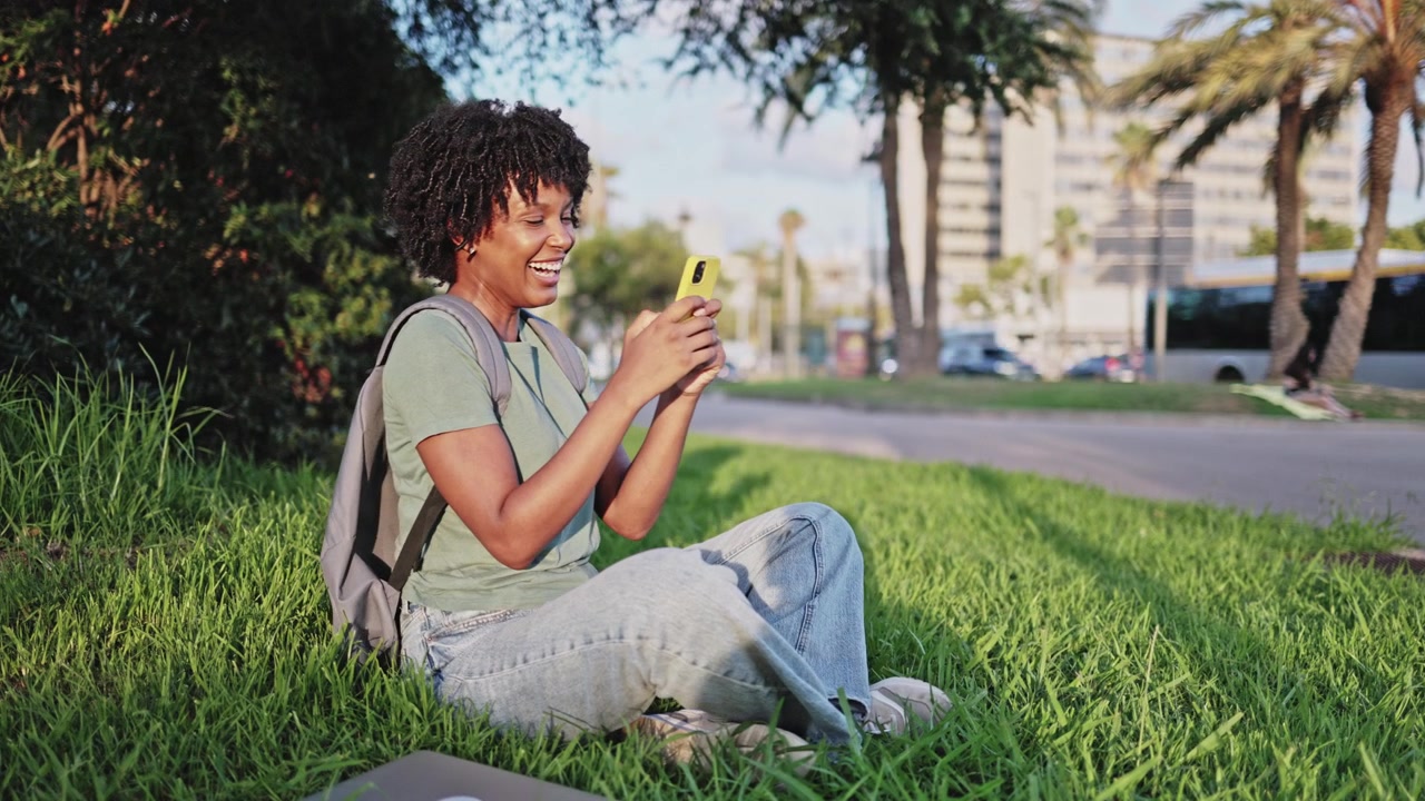 Young African American Woman Laughing While Using Phone on Grass