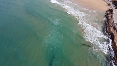 las olas verdes se adentran en una hermosa bahía de arena con un pueblo pintoresco, clima soleado