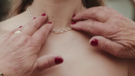 close up of elegant pearls being gently placed on bride’s neckline