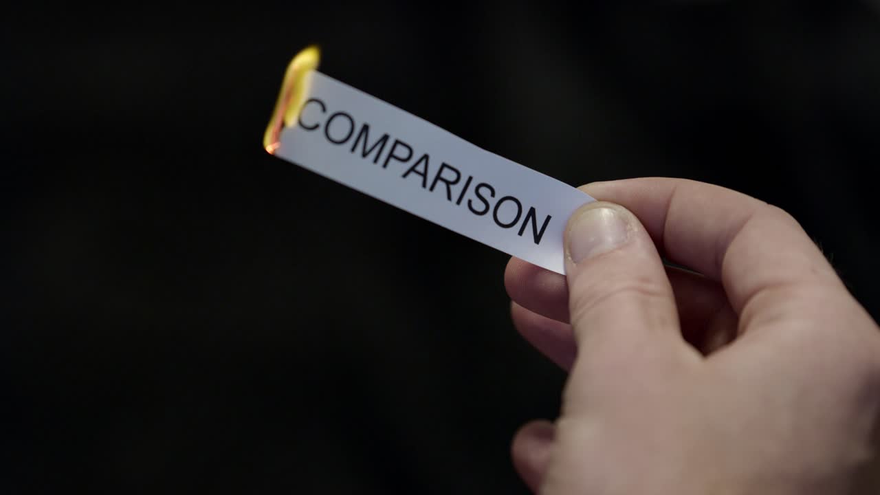 Burning Away Comparison - Hand Setting Fire to Paper note Marked “COMPARISON”, Powerful Release of Criticism, Guilt and Shame, Dark Cinematic Close-Up. Mental health, therapy