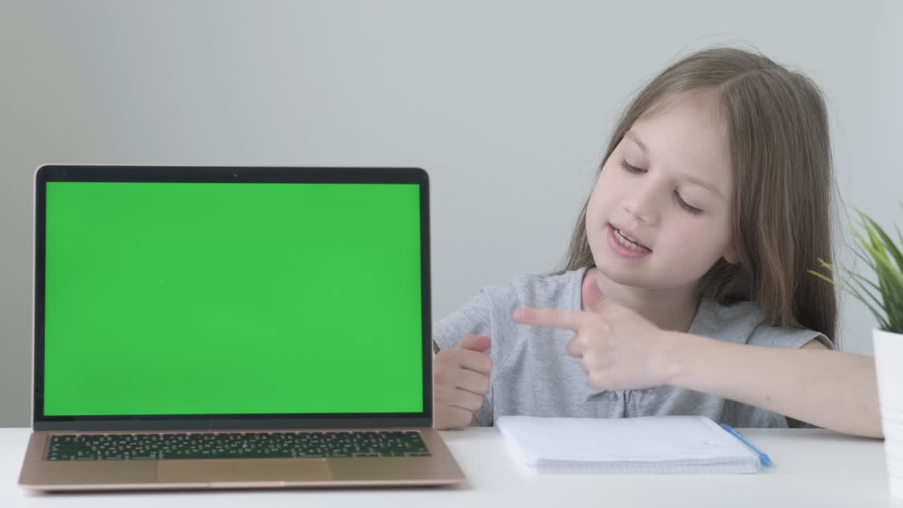 School girl studying homework during online lessons at home. Kid pointing at laptop green screen