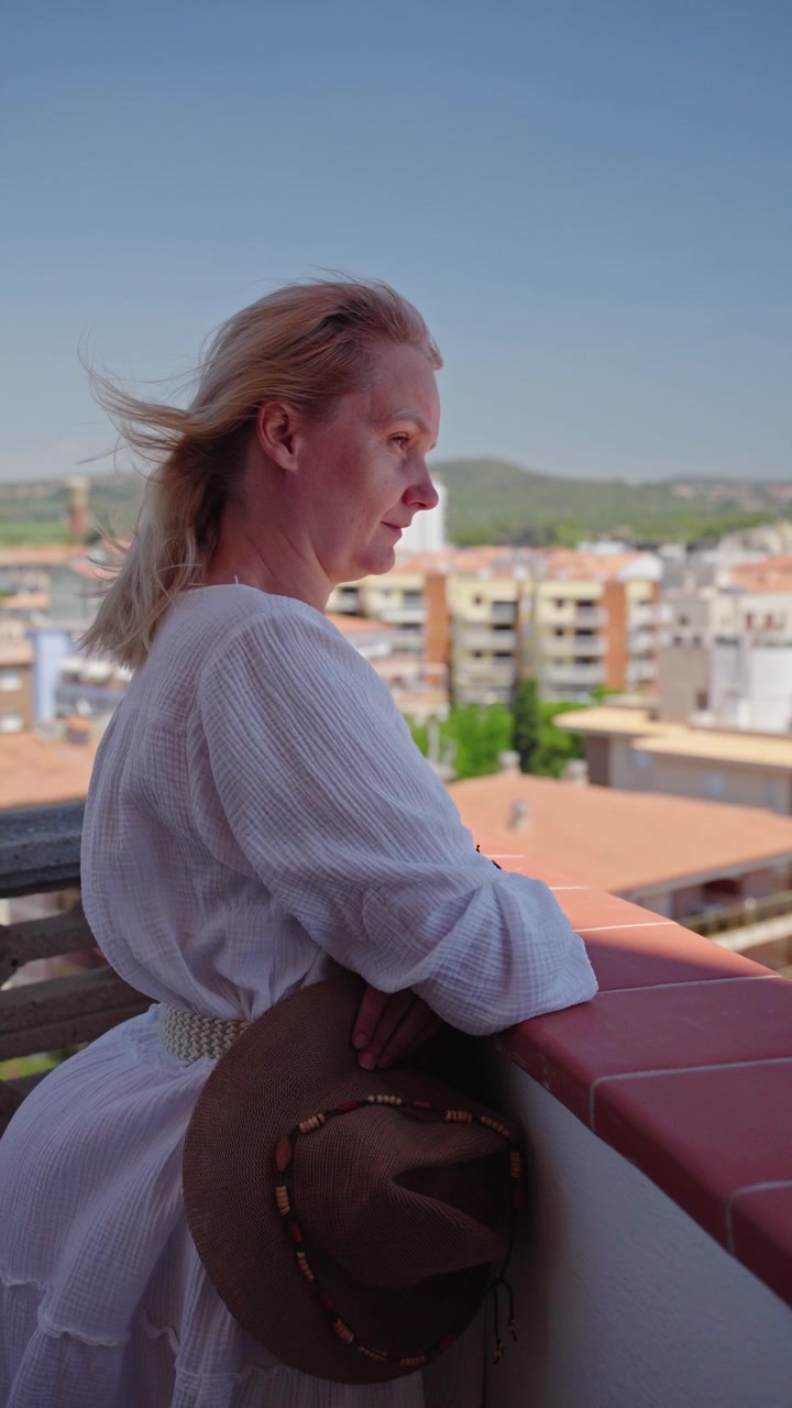 Donna in relax sul balcone di un appartamento con vista panoramica urbana in una calda giornata estiva.
