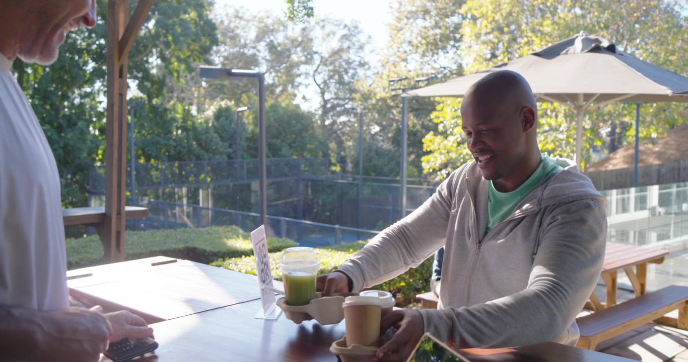 African American man paying on patio as senior server handing reader tapping card lifting carrier