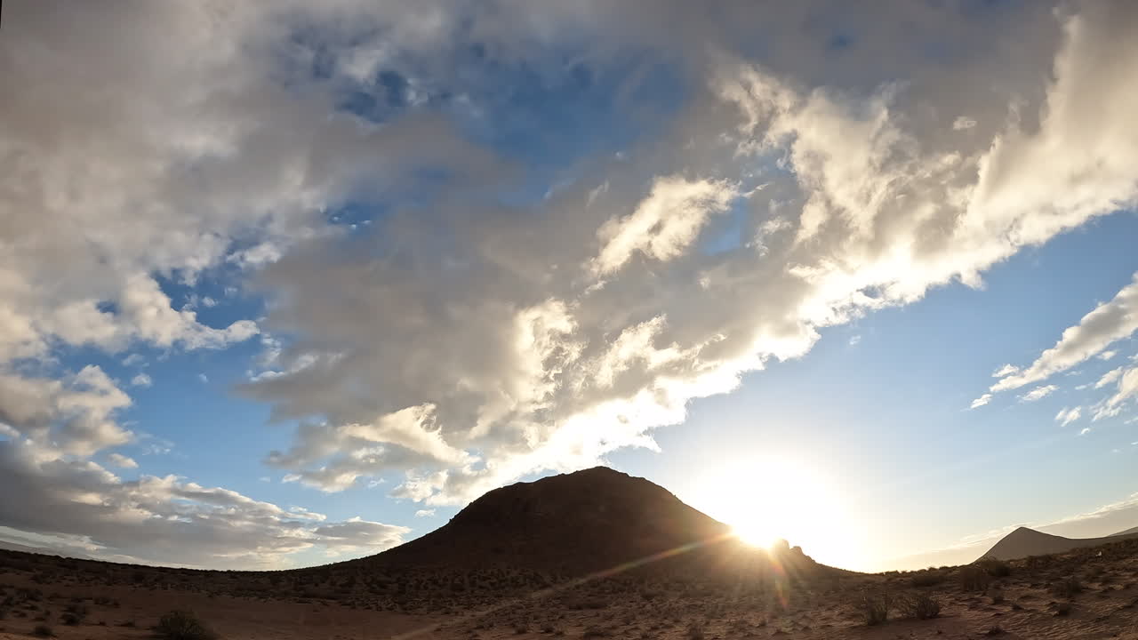 The sun rises above the Mojave Desert with a dynamic cloudscape time lapse over the dome-shaped mountain