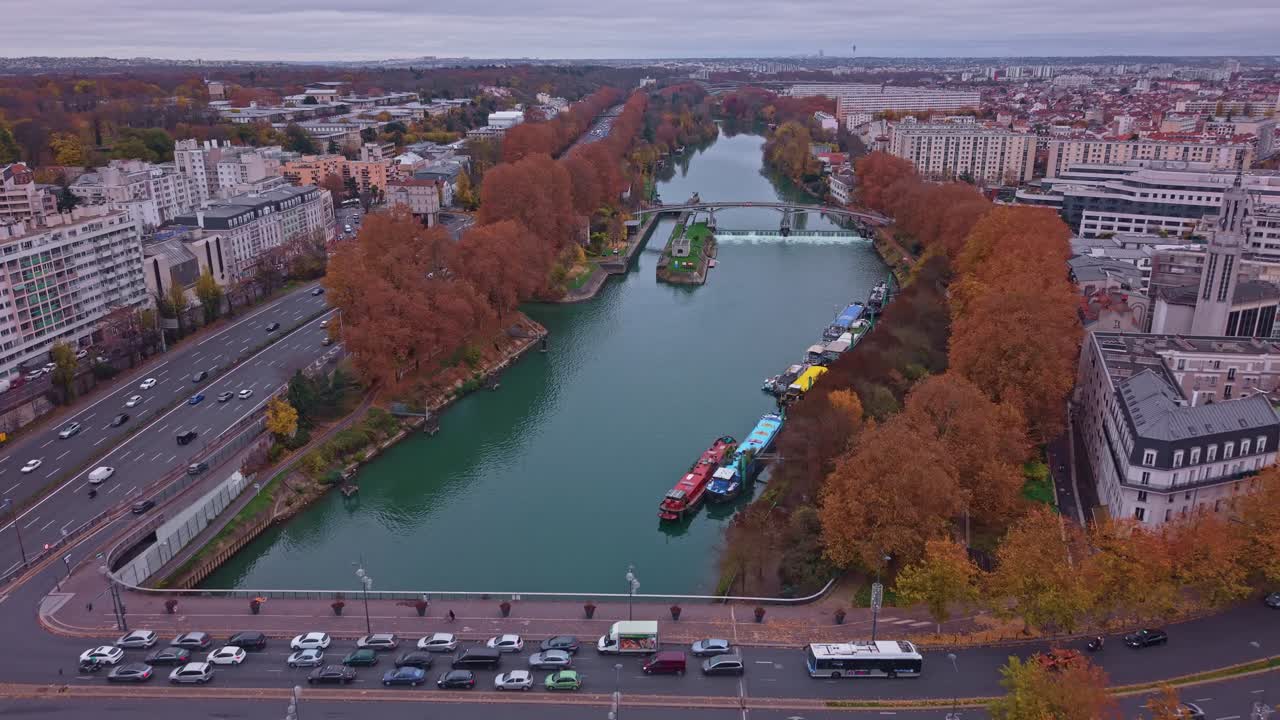 Scenic aerial drone view of the Saint-Maurice lock and dam on the Marne River. Autumn landscape with colorful trees, docked barges, and highway traffic near Paris, France
