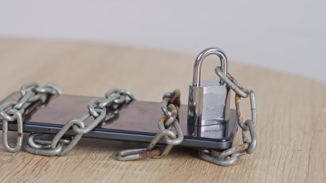 Smartphone secured with metal padlock and rusty chains on wooden surface