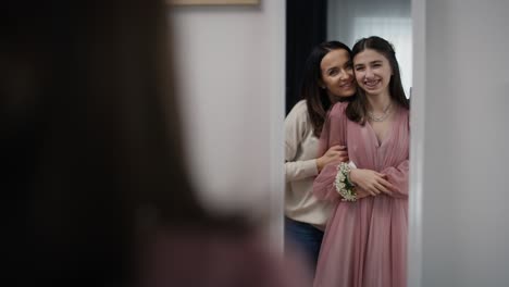 mirror reflection of caucasian mother and daughter in red dress before prom