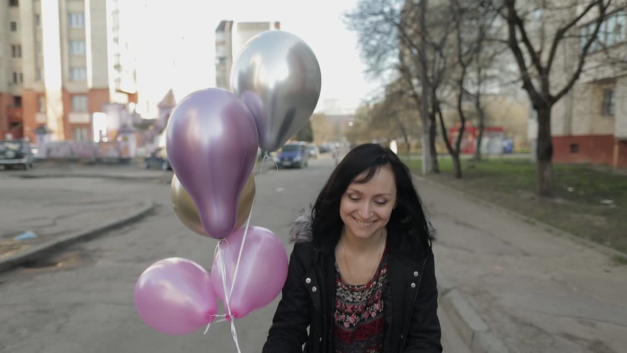 Bella donna che cammina per strada tenendo palloncini ad elio