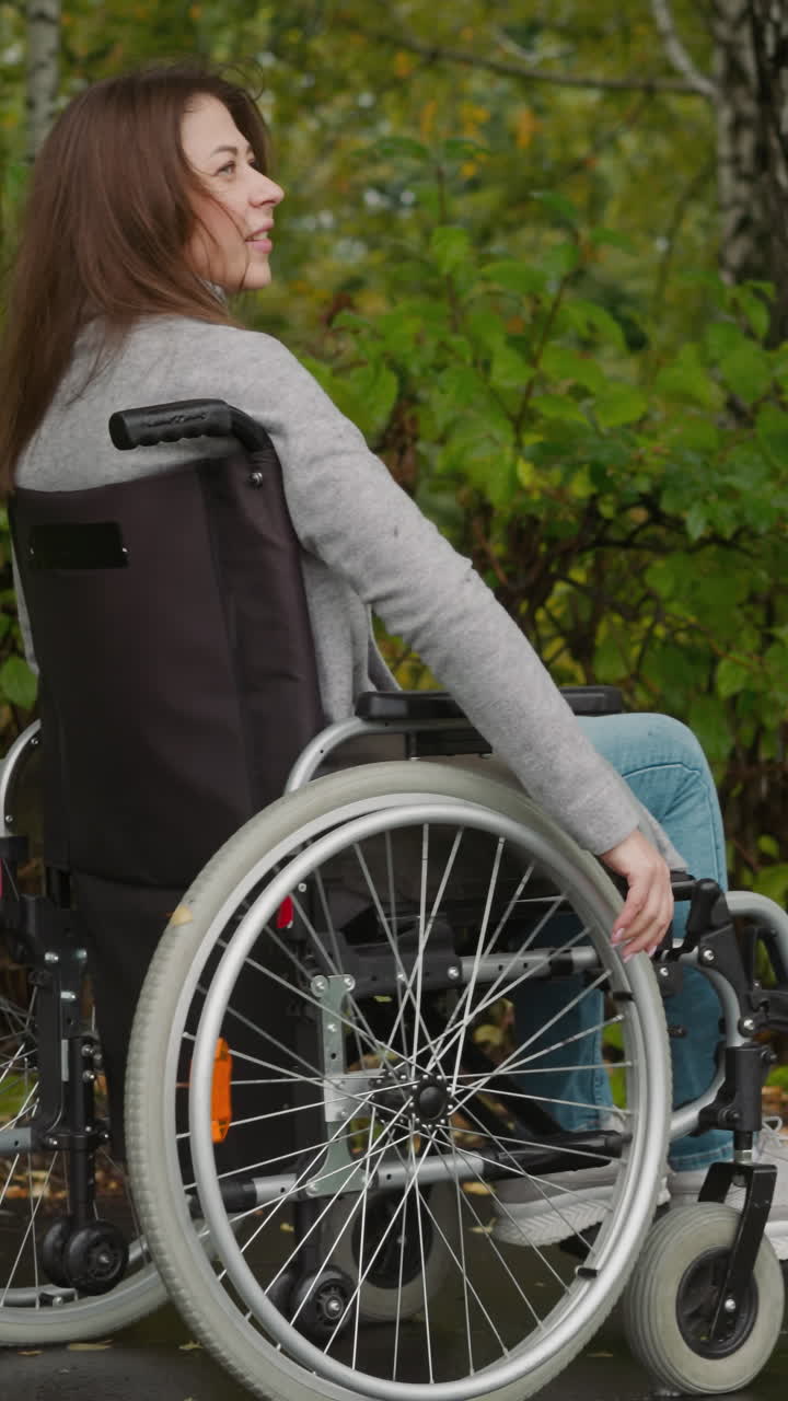 mujer joven con lesiones en las piernas disfruta de la naturaleza a pie. mujer sonriente en silla de ruedas respira profundamente moviéndose en el parque con arbustos viejos vista trasera