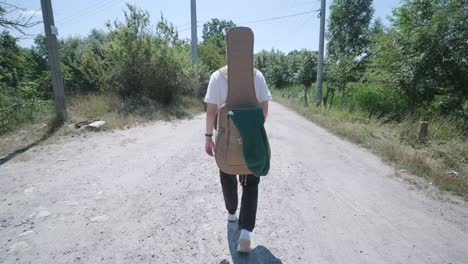 young man walking with guitar on street near forest