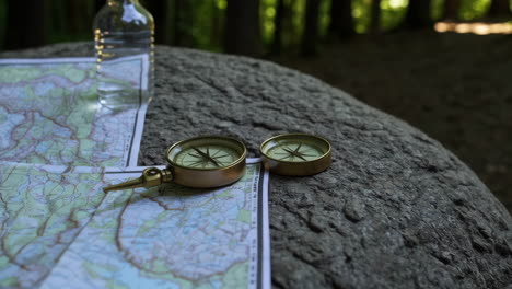hiking map, compass, and water bottle in a forest