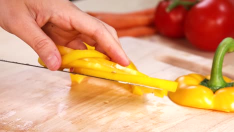 manos cortando pimientos amarillos con tomates y zanahorias