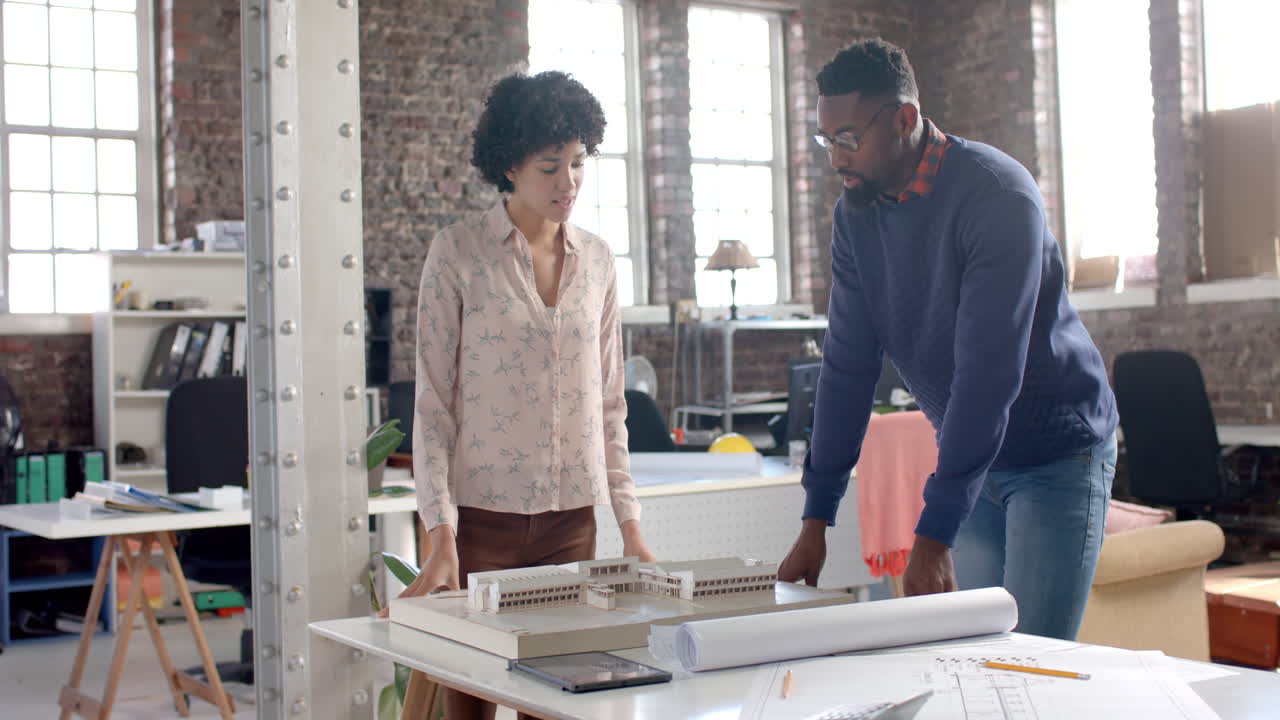 Focused diverse colleagues discussing work at table with building model in office in slow motion