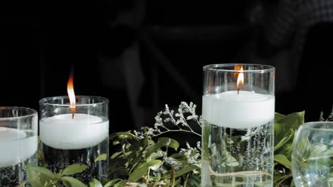 Beautiful-wedding-table-décor-flat-lay-of-white-floating-lit-candles-in-vases-and-green-plants