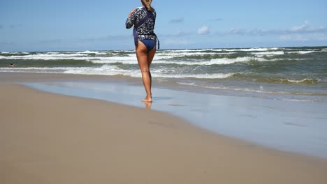 woman walking on beach, carrying a baby in front of her