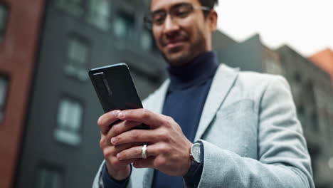hombre sonriendo mientras usa su teléfono en la calle de la ciudad