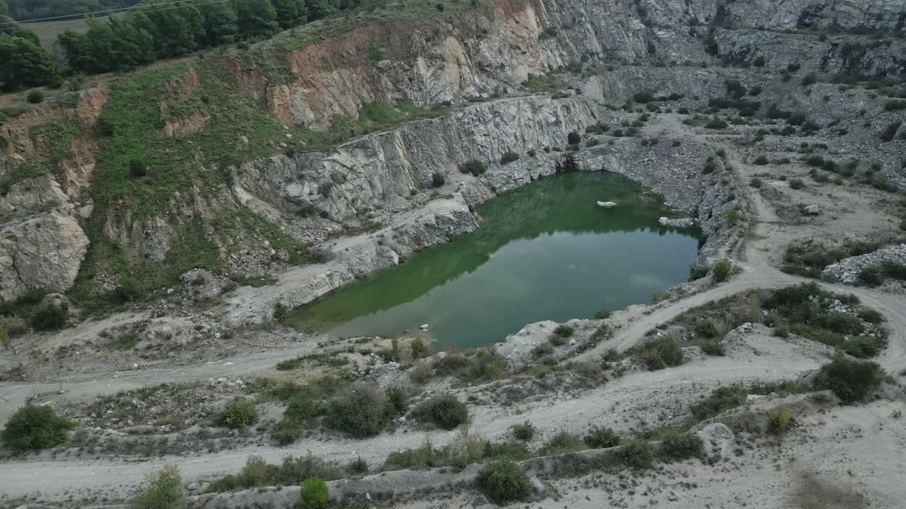 Green, still water has collected at the bottom of an abandoned quarry near sant fost de campsentelles, barcelona, reflecting the surrounding cliffs and vegetation